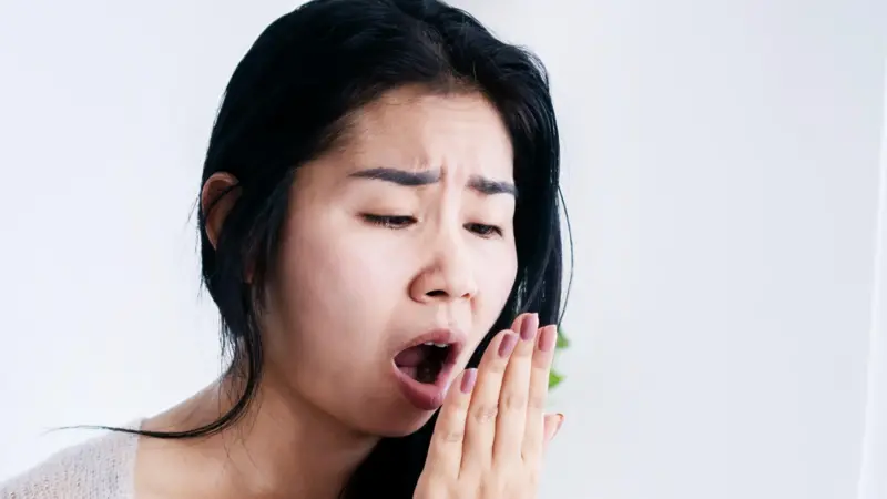 Mutum yana goge haƙora da burushi a gaban madubi don magance warin baki.